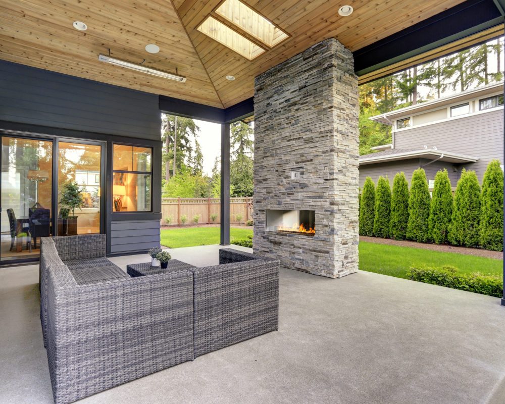 New modern home features a backyard with patio New modern home features a backyard with covered patio accented with stone fireplace, vaulted ceiling with skylights and furnished with gray wicker sofa placed on concrete floor. Northwest, USA