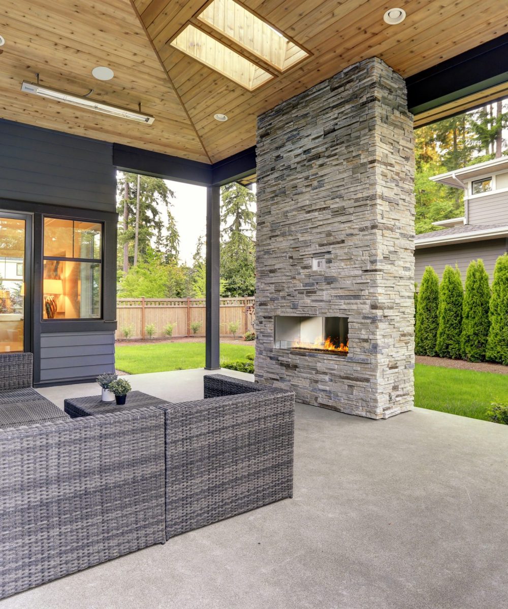 New modern home features a backyard with patio New modern home features a backyard with covered patio accented with stone fireplace, vaulted ceiling with skylights and furnished with gray wicker sofa placed on concrete floor. Northwest, USA